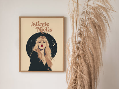 A framed poster of Stevie Nicks features her portrait with a celestial background, including stars and a crescent moon, next to decorative dried pampas grass.