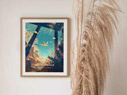 A framed minimalist poster of Dry Tortugas National Park features an underwater scene with colorful fish and corals. It hangs on a wall beside tall, dried decorative grasses.