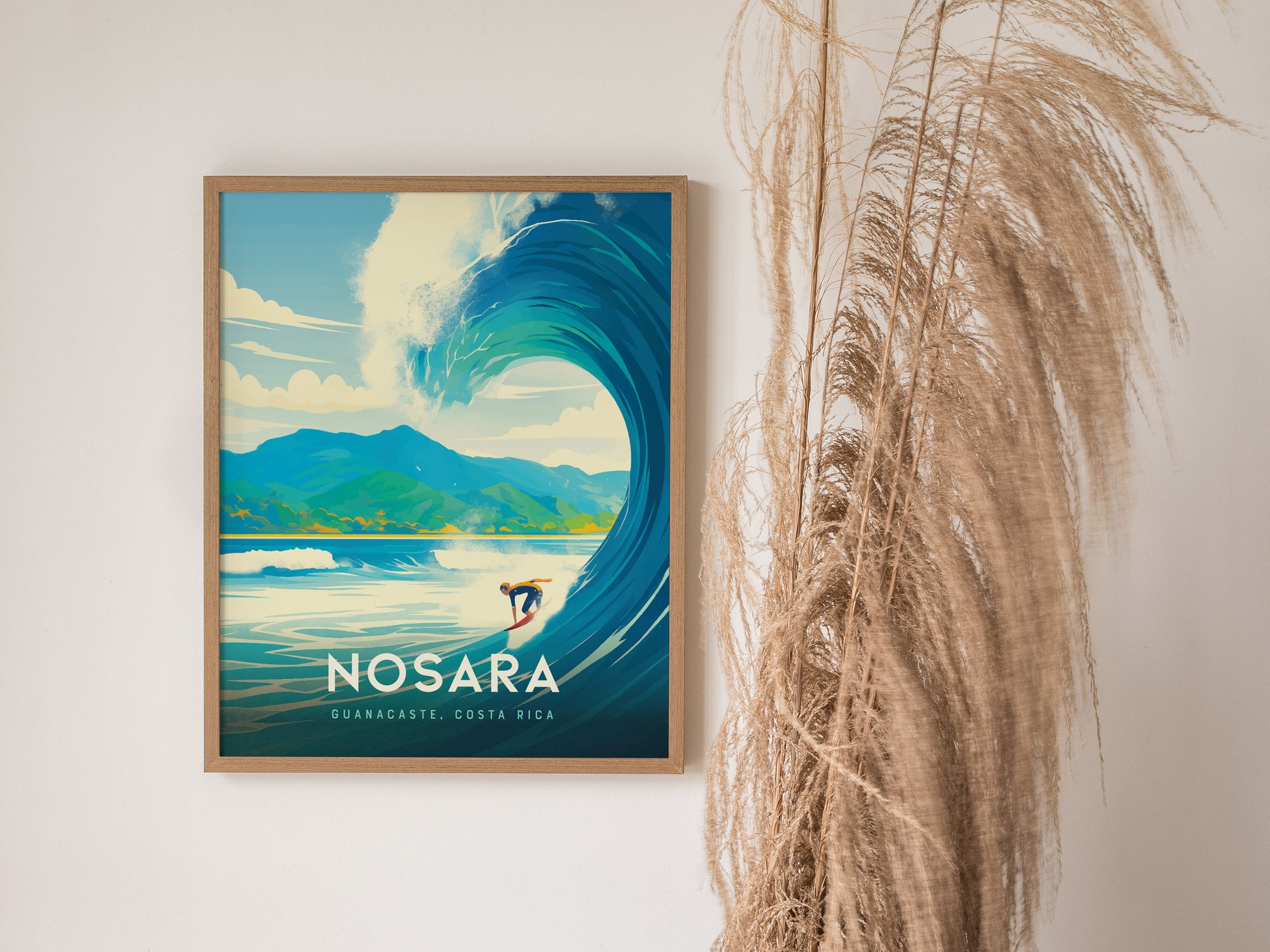 Framed poster of a surfer riding a large wave with mountains in the background, labeled Nosara, Guanacaste, Costa Rica, next to decorative dried grasses.
