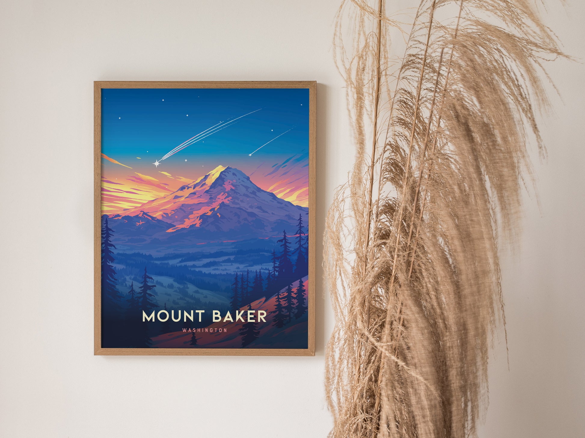 A framed Mount Baker poster showcases a vibrant sunset over the mountain, with shooting stars in the sky. Its displayed next to decorative dried pampas grass.