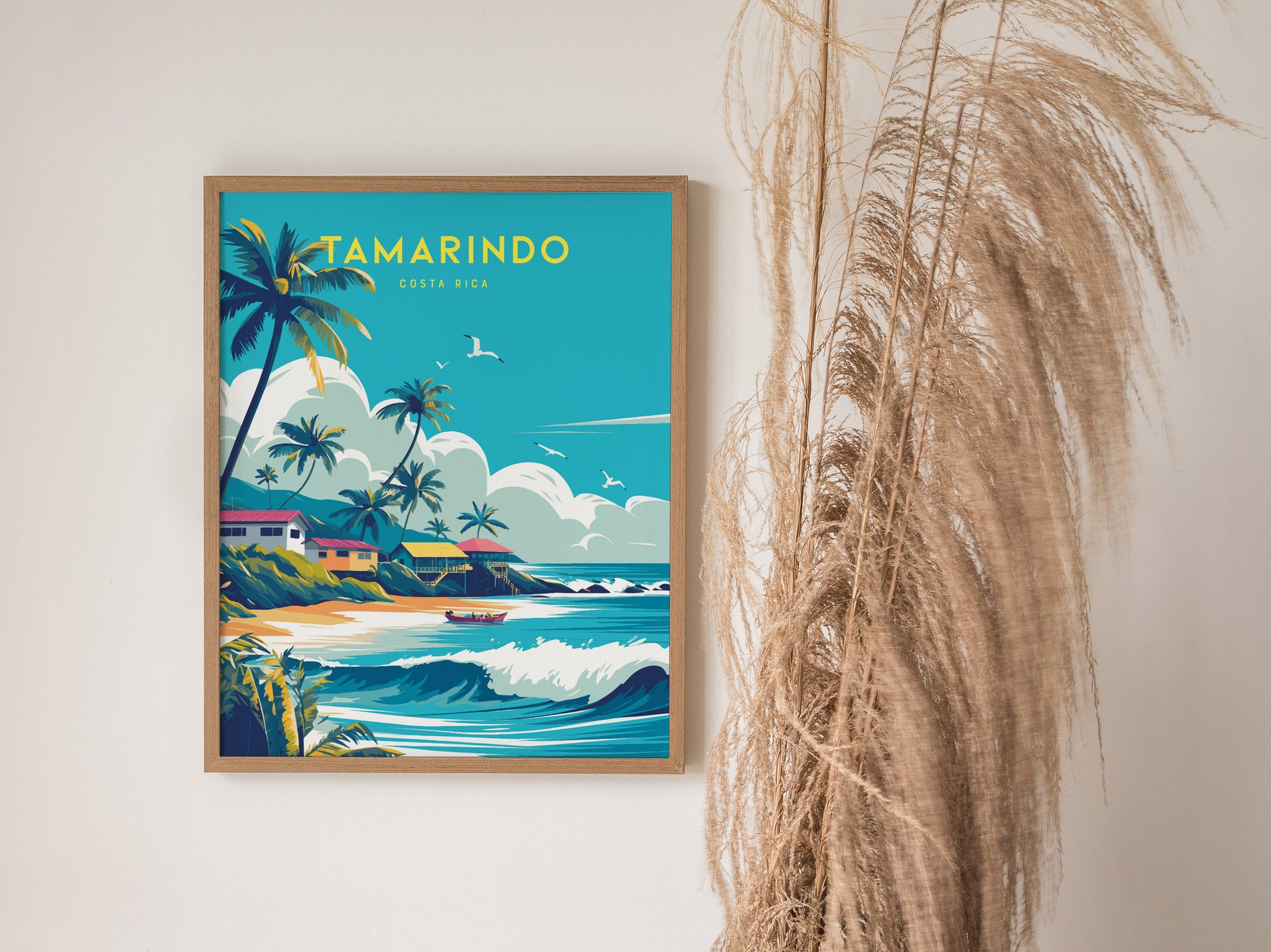 A framed poster features vibrant artwork of a tropical beach scene with palm trees and waves, titled Tamarindo Costa Rica. It is displayed next to dried pampas grass.