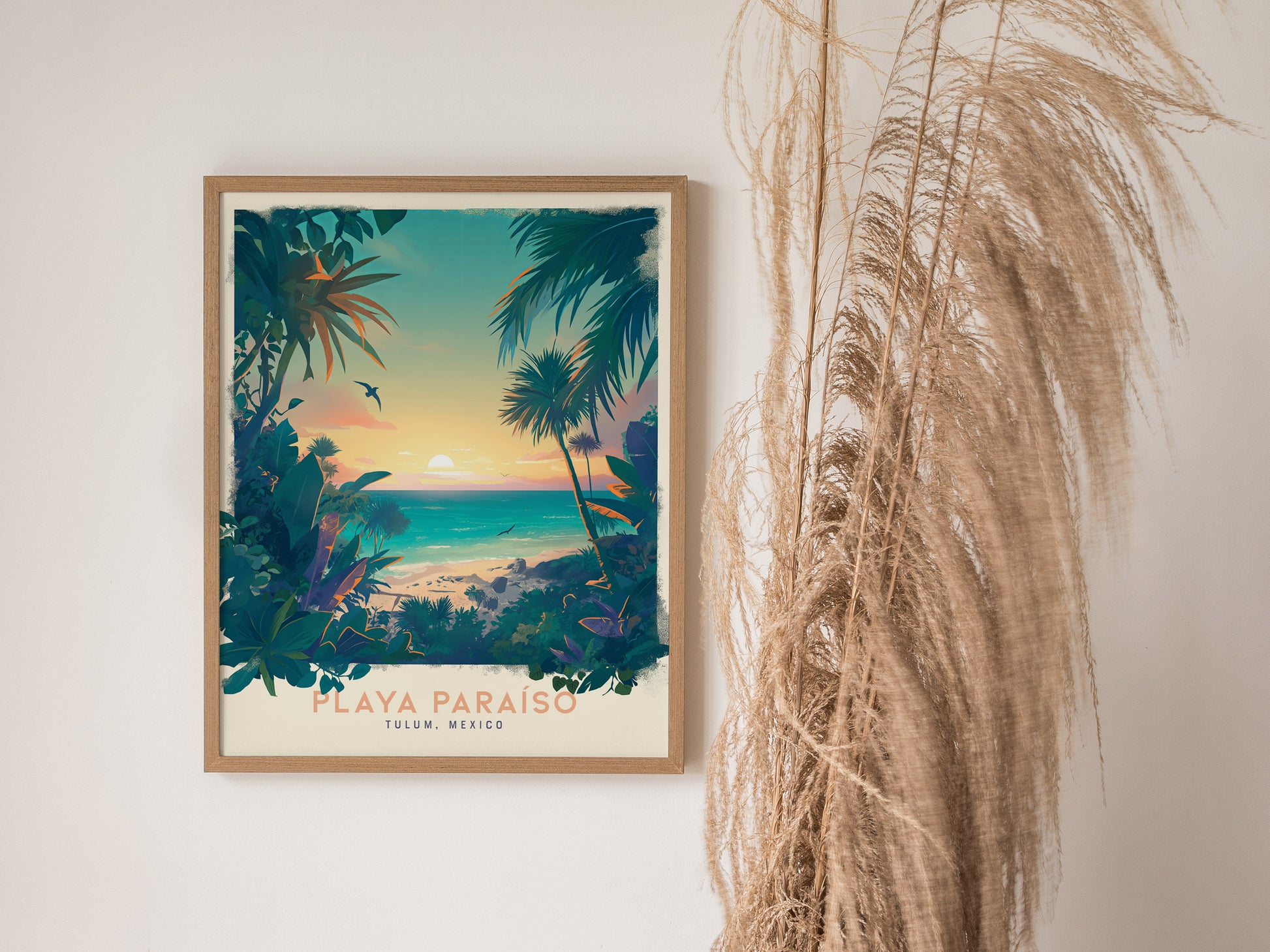 A framed poster of Playa Paraiso, Tulum, featuring a vibrant beach scene with palm trees, a colorful sunset, and turquoise waters, is displayed next to dried pampas grass.