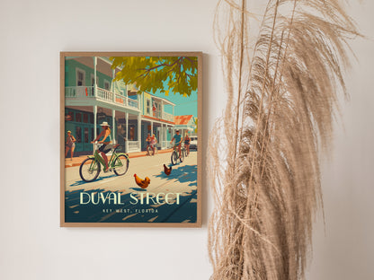 A framed poster of Duval Street in Key West shows people biking alongside roosters under a sunny sky, with vibrant buildings in the background.