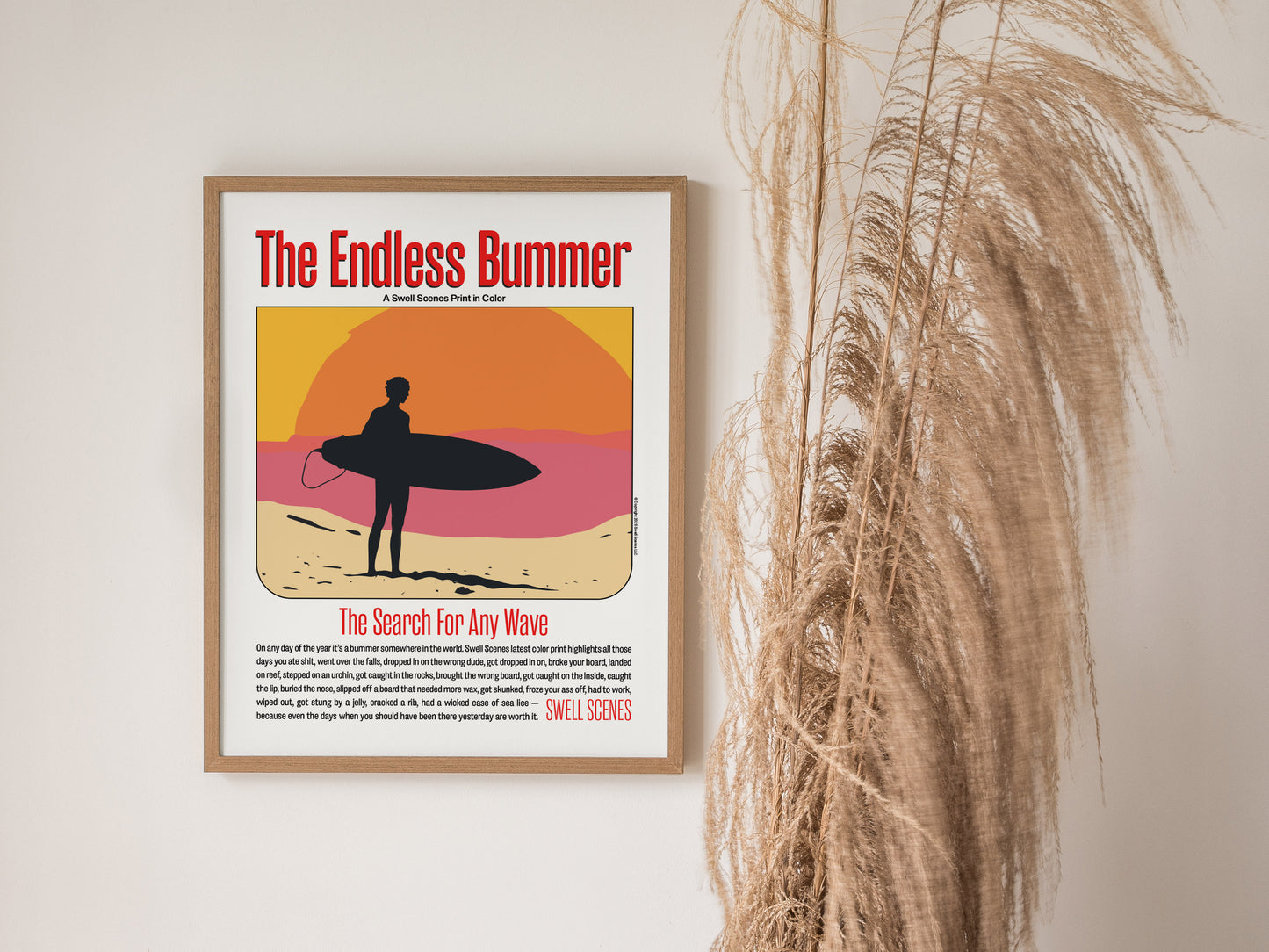 A framed poster titled The Endless Bummer features a silhouetted surfer against a vibrant sunset. It hangs on a wall next to tall, dried grasses.