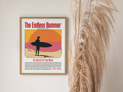 A framed poster titled The Endless Bummer features a silhouetted surfer against a vibrant sunset. It hangs on a wall next to tall, dried grasses.