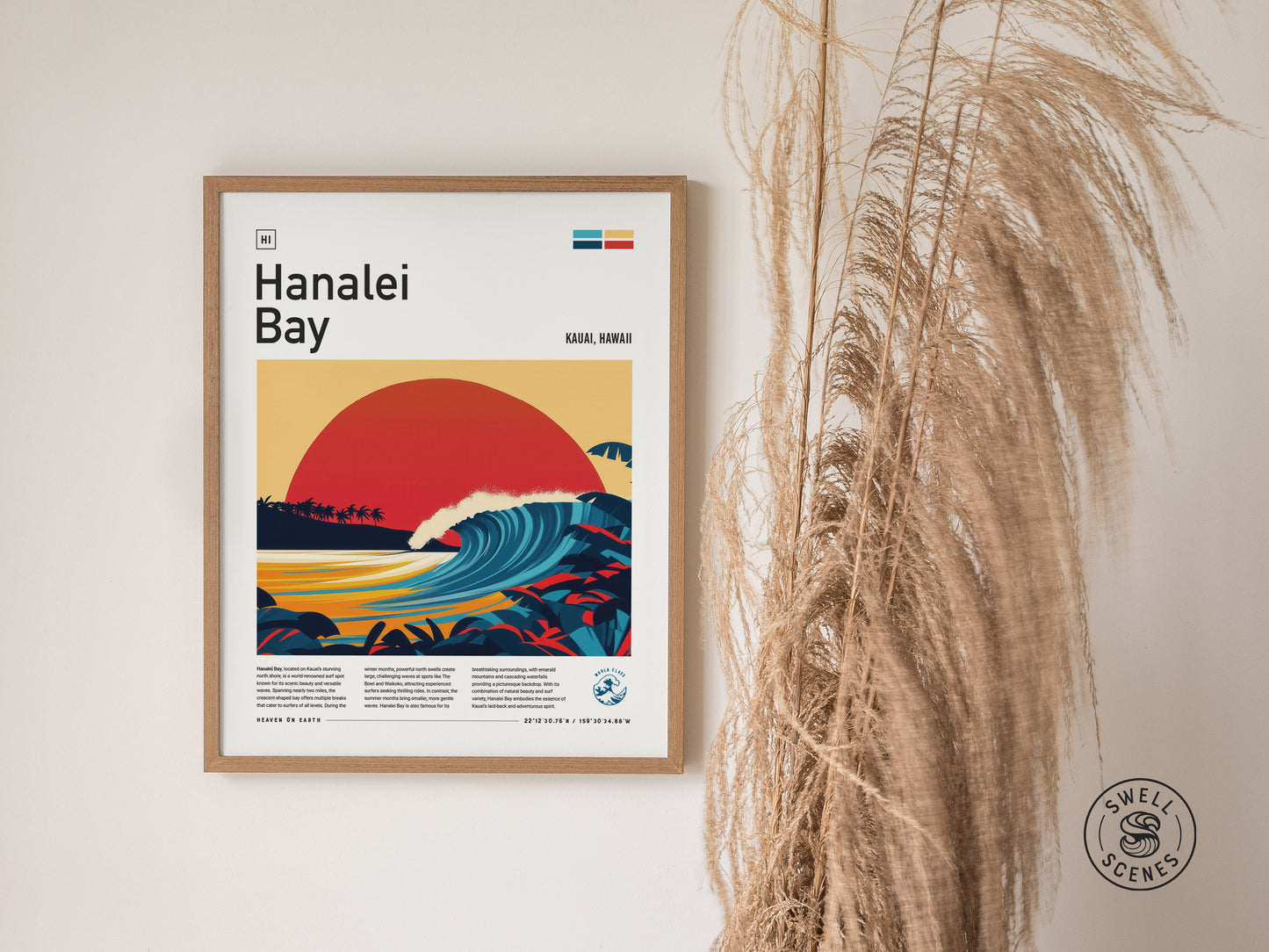 Framed Hanalei Bay poster depicting a vibrant, stylized sunset over a curling wave, surrounded by tropical foliage. The artwork is displayed on a wall next to dried pampas grass.