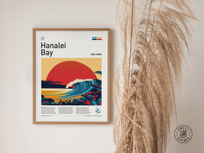 Framed Hanalei Bay poster depicting a vibrant, stylized sunset over a curling wave, surrounded by tropical foliage. The artwork is displayed on a wall next to dried pampas grass.