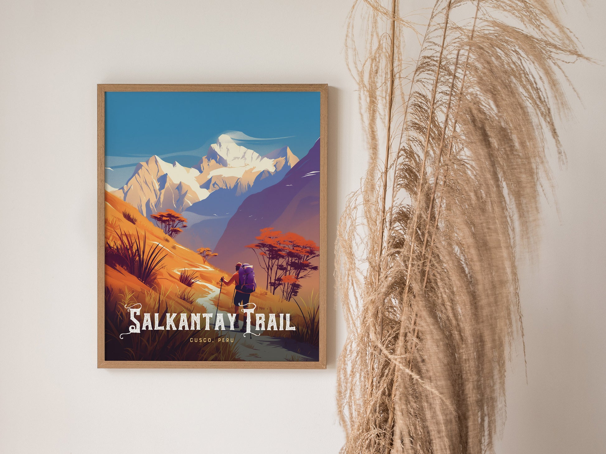 A framed poster of the Salkantay Trail featuring vibrant, colorful mountains and a hiker, with decorative grasses positioned nearby on a plain wall.