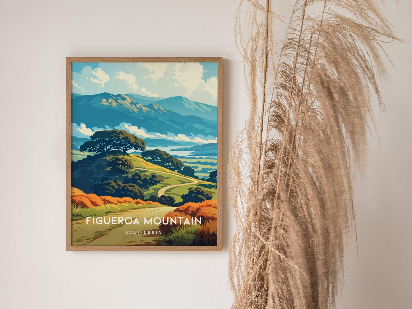 A framed poster of Figueroa Mountain in California features a vibrant landscape with rolling hills, lush greenery, and distant mountains under a blue sky. The artwork is complemented by decorative pampas grass positioned nearby.
