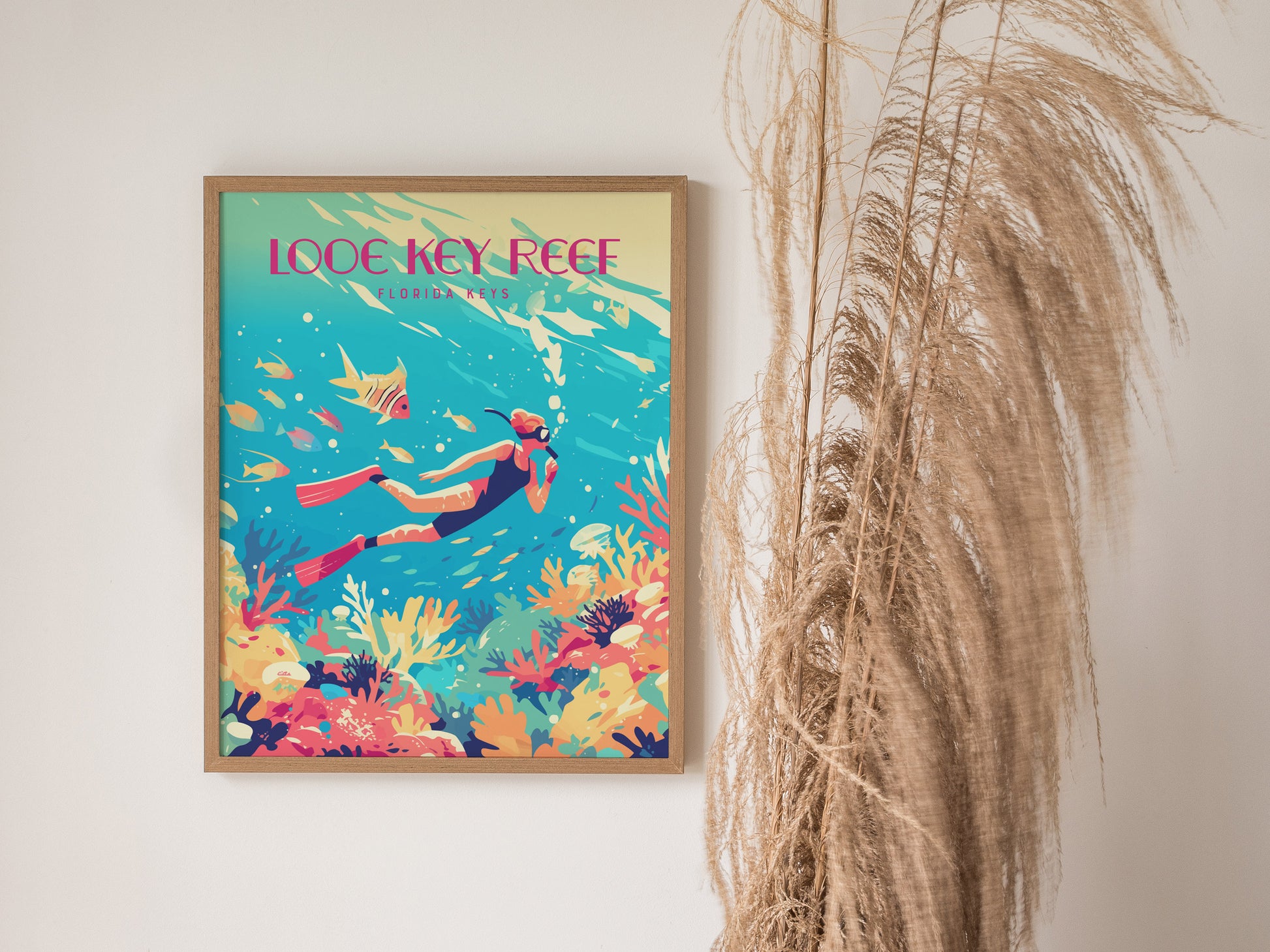 A framed poster of a diver exploring a colorful coral reef with fish is displayed on a wall, next to tall, dried grasses.