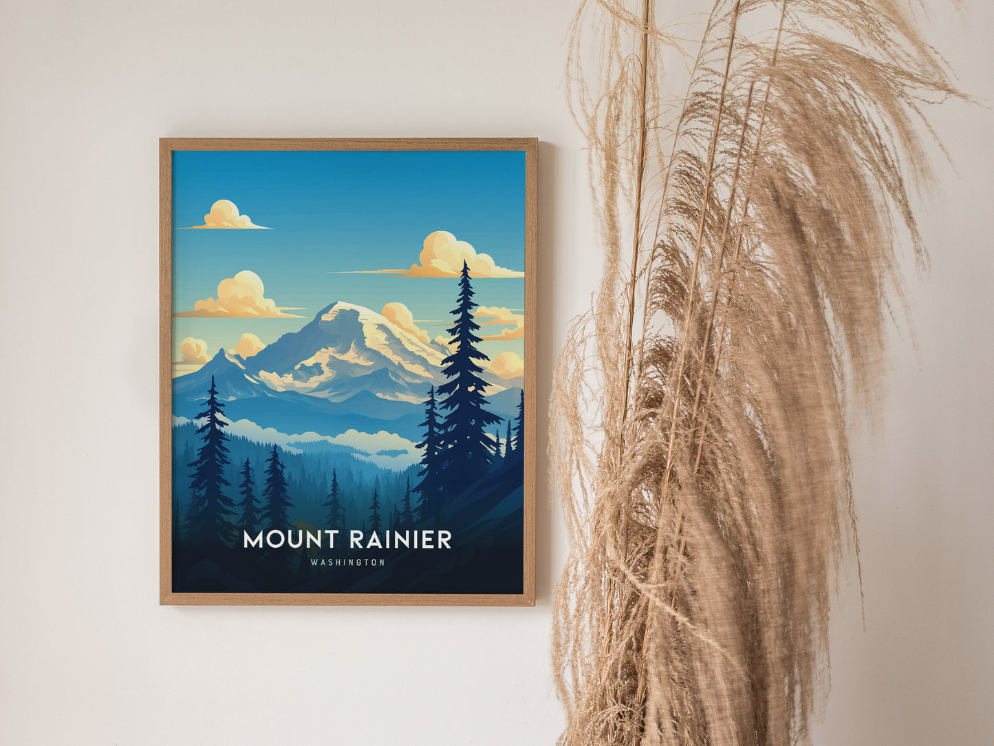 A framed poster of Mount Rainier with a blue sky, fluffy clouds, and evergreen trees is displayed on a wall next to dried pampas grass.