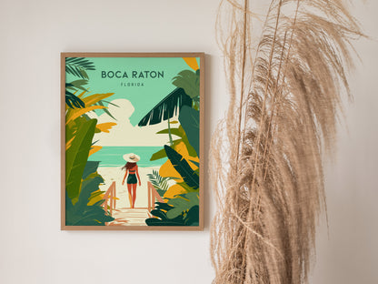 A framed Boca Raton travel print depicts a woman walking towards the beach, surrounded by tropical greenery. The art hangs beside dried ornamental grasses.