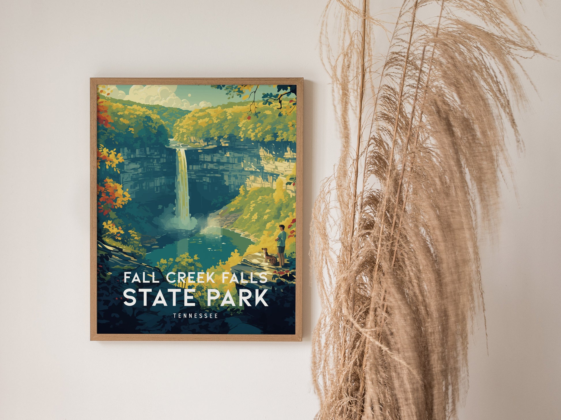 A framed poster of Fall Creek Falls State Park, featuring a vibrant illustration of the waterfall surrounded by lush greenery, is displayed on a wall beside tall, wispy dried grass.
