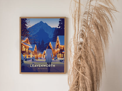 Framed poster of Leavenworth, Washington, featuring a snowy village with illuminated buildings and mountains in the background. The poster is displayed on a wall beside tall dried grasses.
