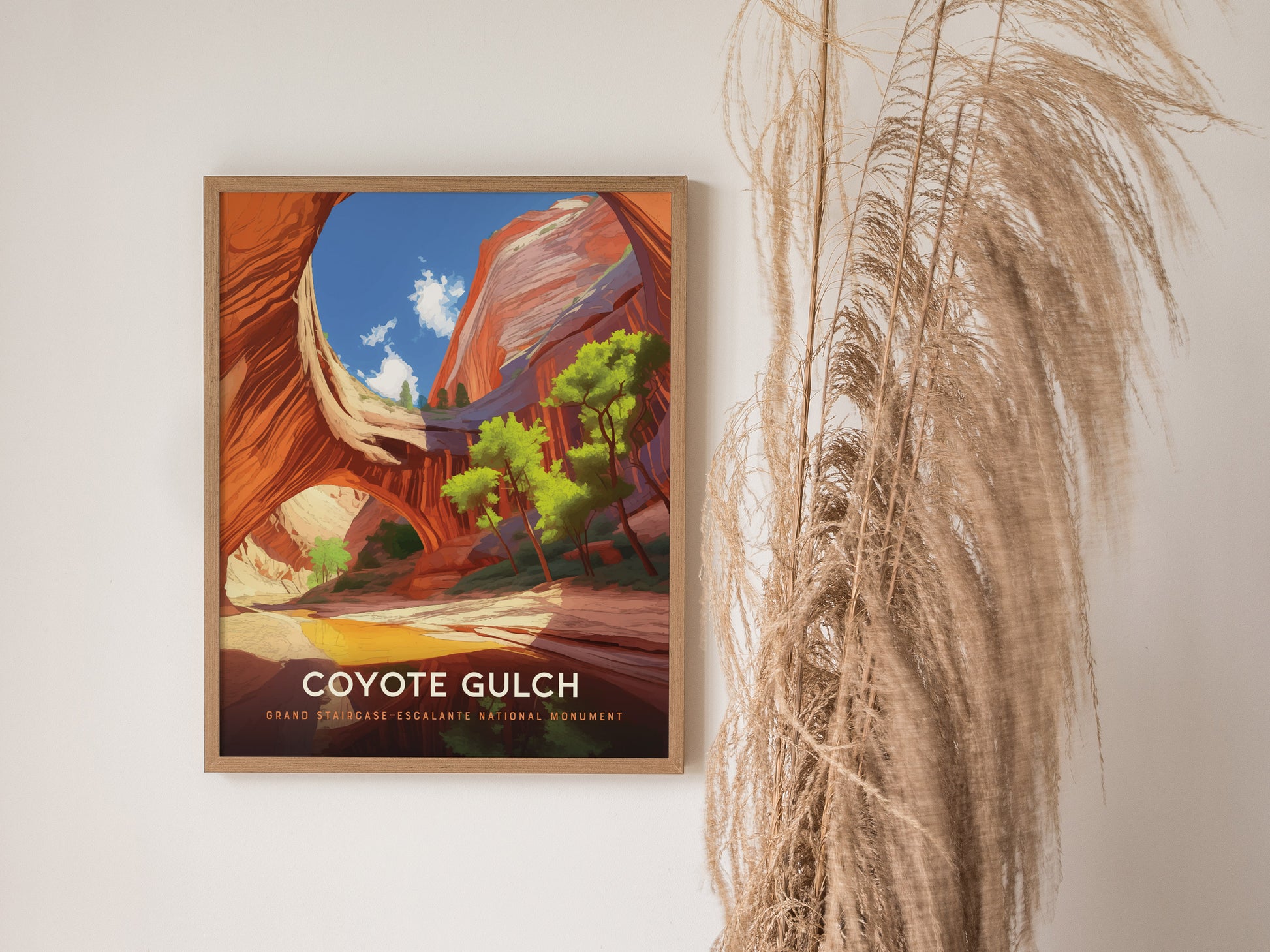 A framed poster of Coyote Gulch is displayed on a white wall, featuring vibrant canyon scenery with blue skies. Dried pampas grass decorates the space beside it.