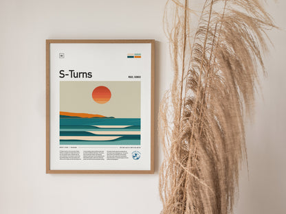 A framed S-Turns Maui poster features minimalist artwork of a sunset over ocean waves, with pampas grass decor placed beside it.
