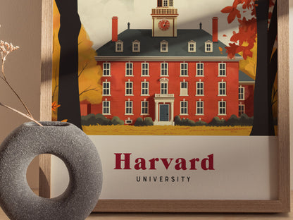 Framed poster of a red-brick building with a clock tower, surrounded by autumn trees, labeled Harvard University. A gray circular vase with dried flowers is in the foreground.