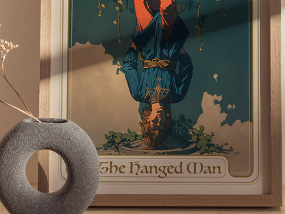 A framed Hanged Man tarot card poster shows a serene figure suspended upside down, surrounded by vines. A round stone vase with dried flowers is in the foreground.