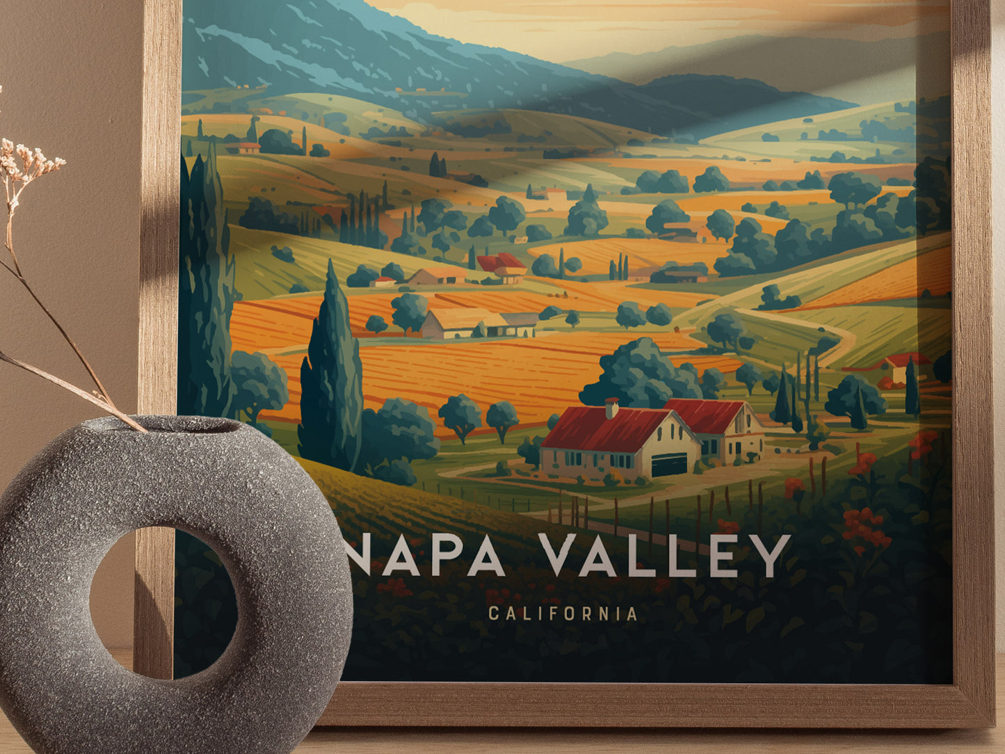 A framed Napa Valley poster depicts rolling vineyards, tree-lined hills, and a farmhouse under warm sunset tones. A ceramic vase with dried flowers is partially visible beside it.