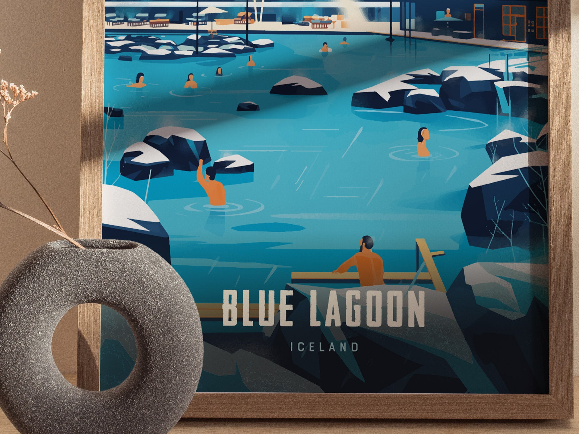 A framed poster of Blue Lagoon, Iceland, shows people enjoying a geothermal spa surrounded by black rocks and milky blue water. A decorative vase is placed nearby.