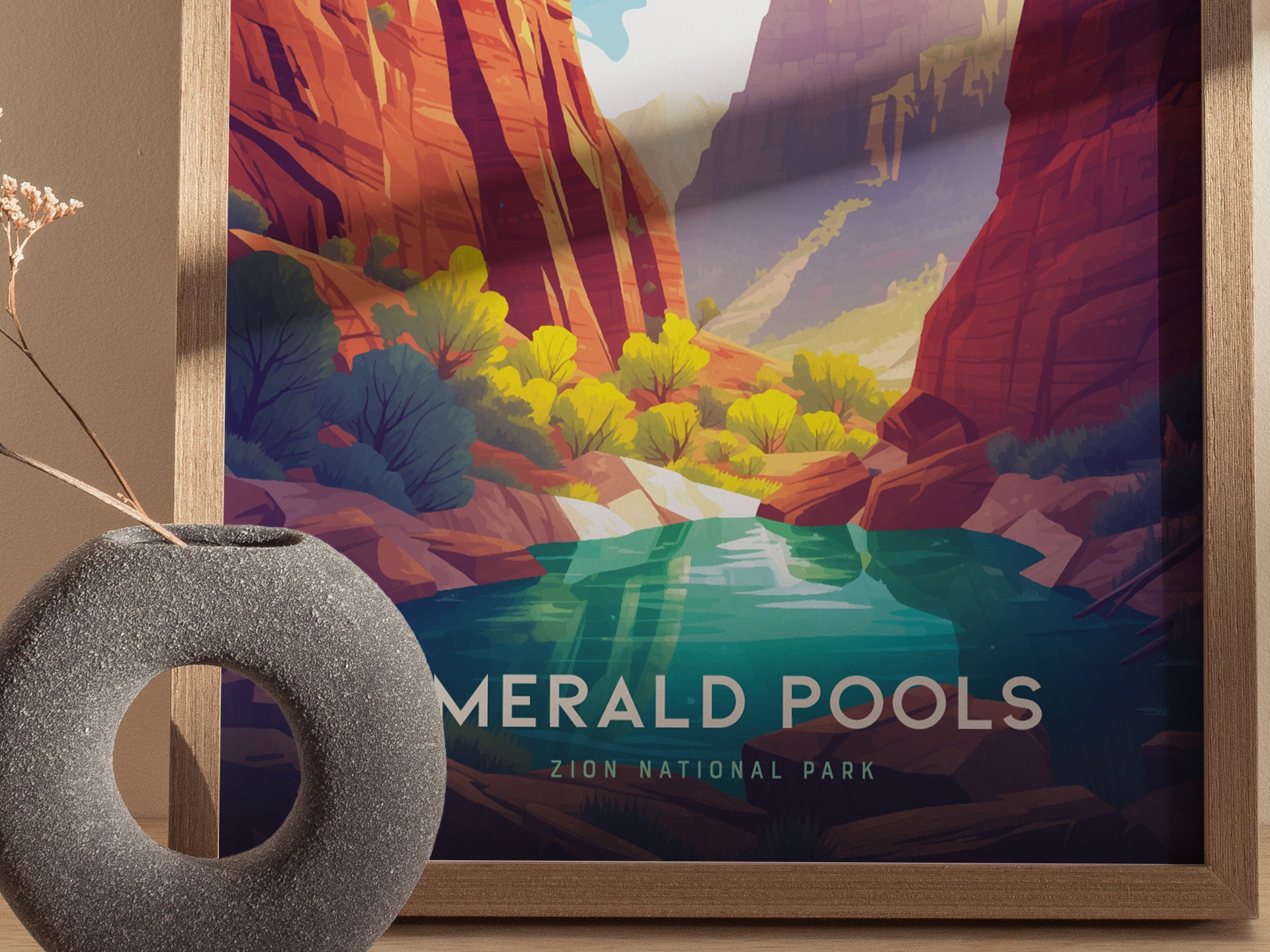 A framed poster of Zion National Parks Emerald Pools featuring vibrant canyon cliffs and a tranquil pool, with a textured stone vase and dried flowers in the foreground.
