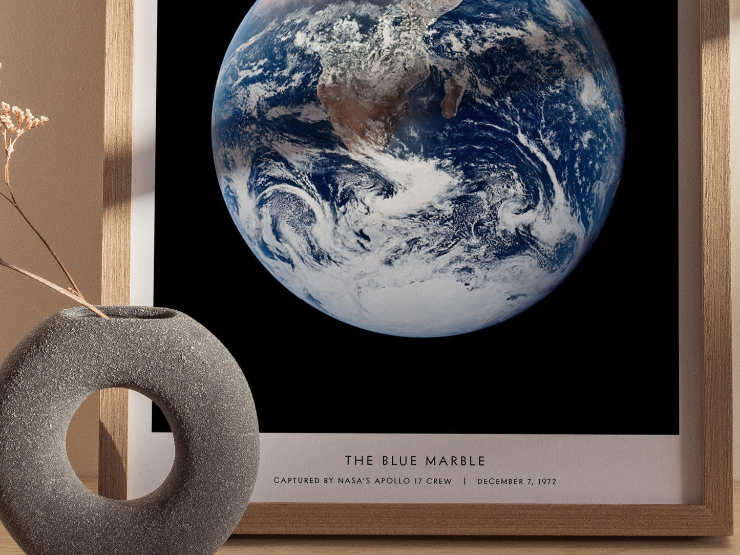 Framed print of 'The Blue Marble' Earth image with decorative vase on a table.