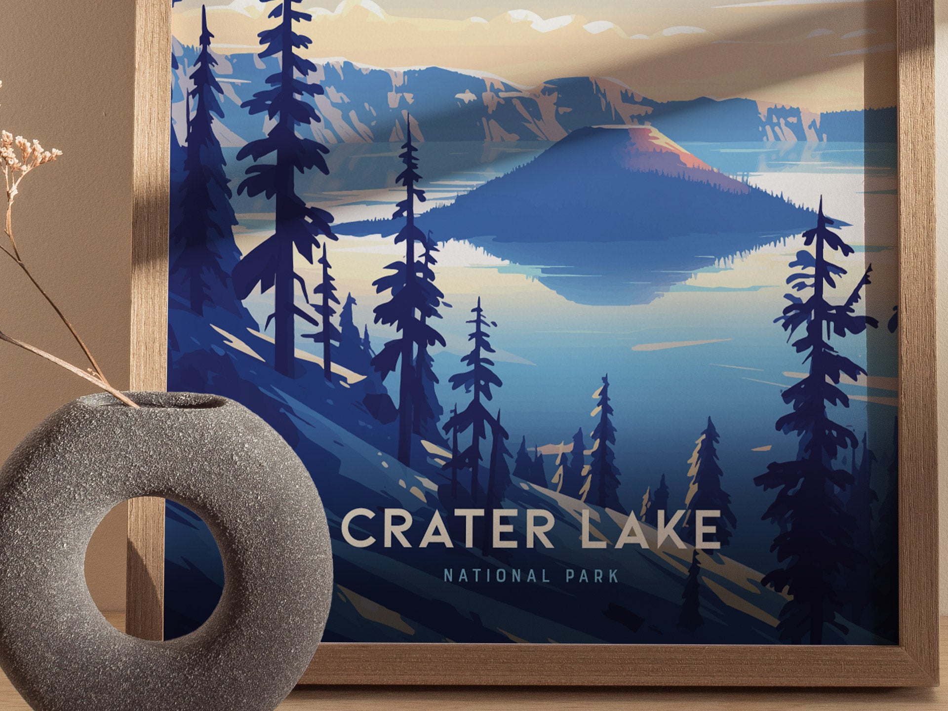 A framed poster of Crater Lake National Park features a vibrant illustration of the lakes mirror-like surface and surrounding volcanic cliffs, with silhouetted trees in the foreground.