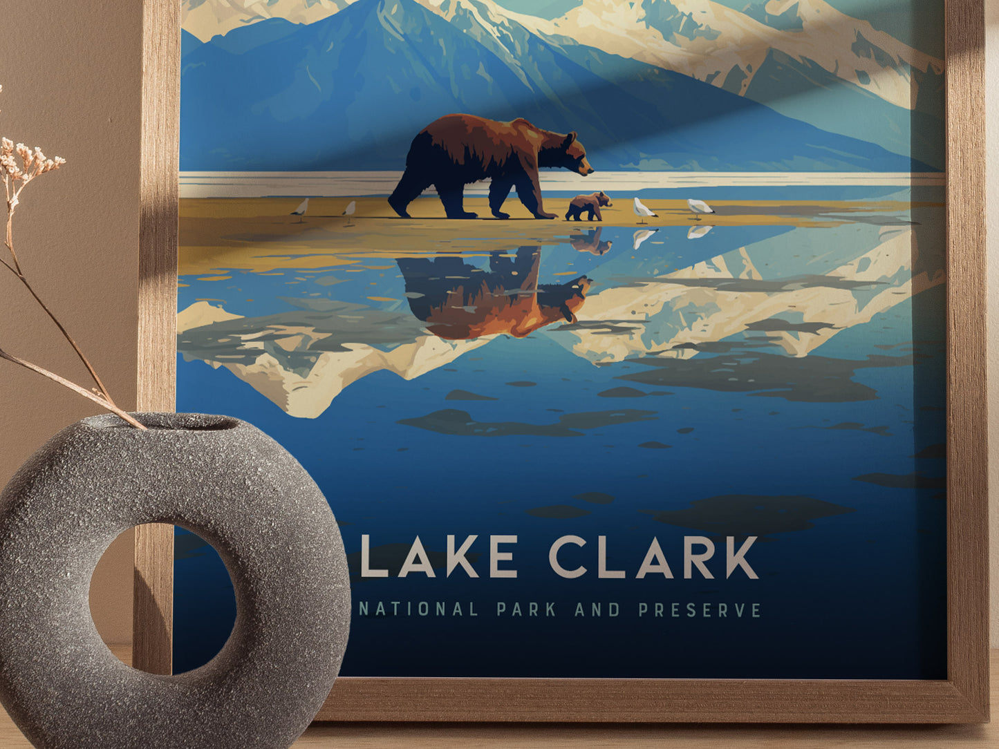 A framed poster of Lake Clark National Park features a bear and cub walking along a reflective lake, with mountains in the background. A textured vase sits nearby.