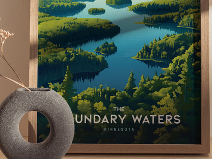 Framed poster of Boundary Waters in Minnesota featuring vibrant green forested shorelines and calm blue waters. A textured gray vase with dried flowers is placed beside it.