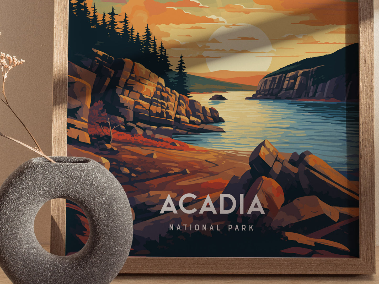 A framed illustration of Acadia National Park shows a vibrant sunset over rocky cliffs and a serene coastline, with a textured vase in the foreground.
