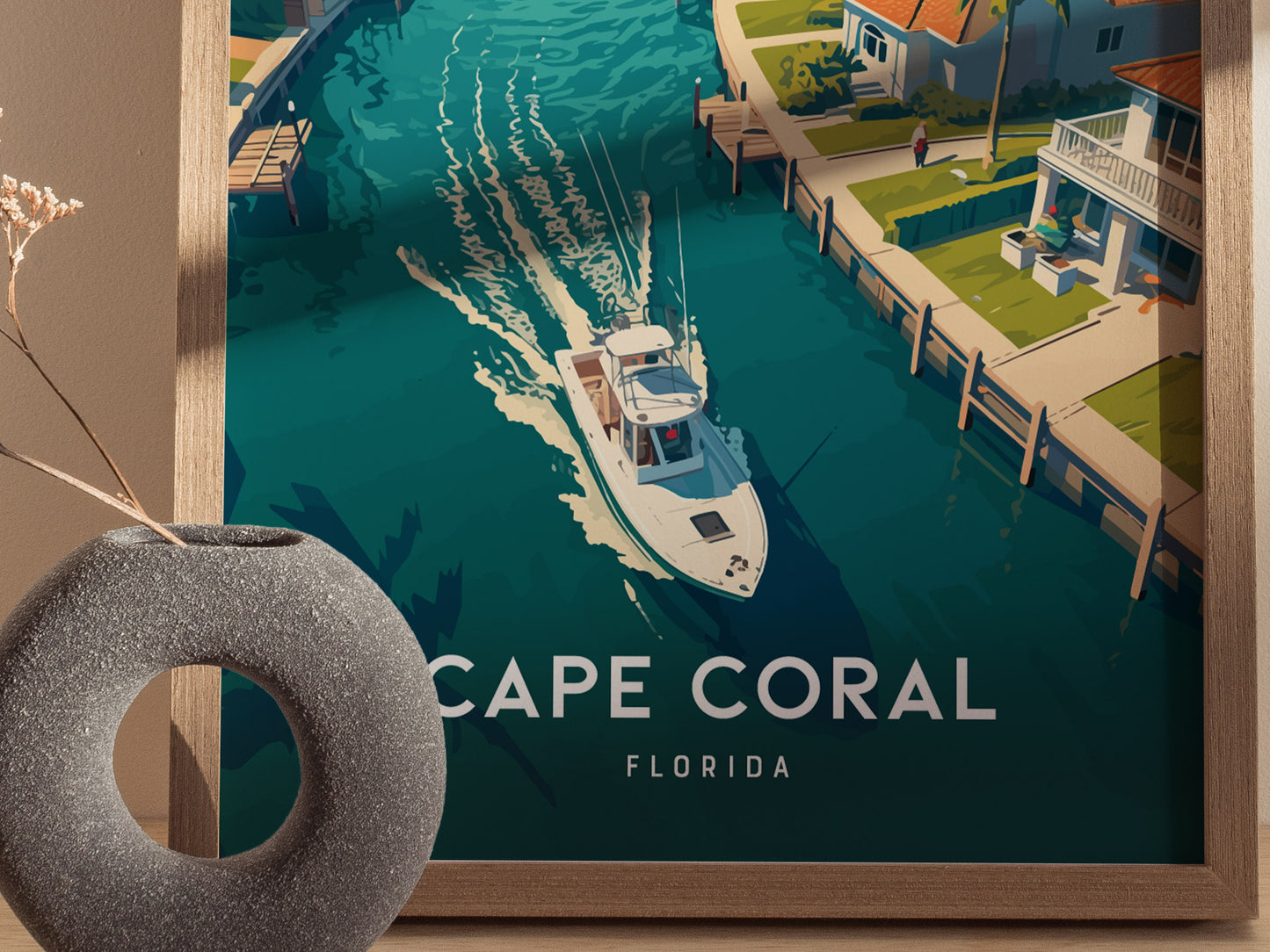 A framed poster features a vibrant illustration of a boat navigating a canal lined with tropical homes in Cape Coral, Florida. A decorative vase is visible in the foreground.