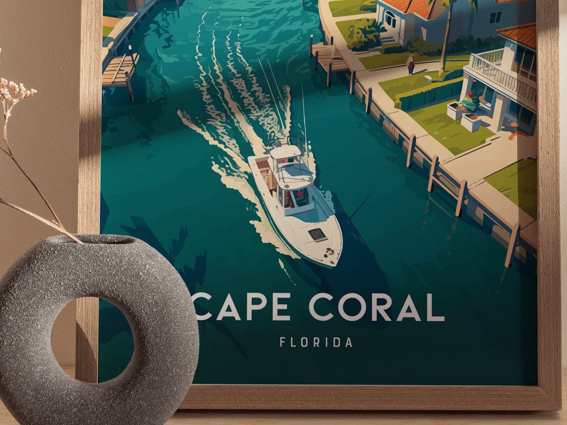 A framed poster features a vibrant illustration of a boat navigating a canal lined with tropical homes in Cape Coral, Florida. A decorative vase is visible in the foreground.