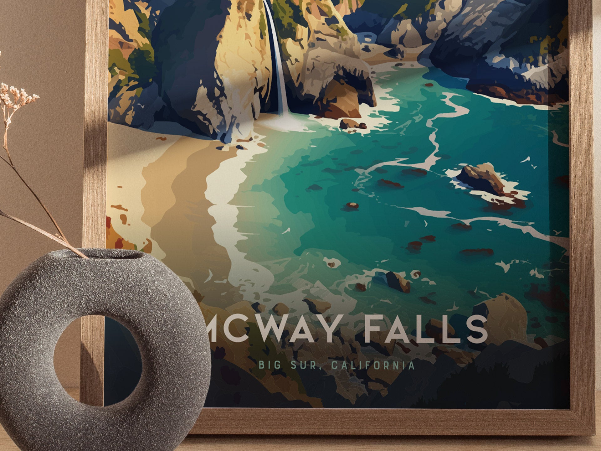 A framed poster of McWay Falls in Big Sur, California, is displayed alongside a circular stone vase. The artwork features a turquoise cove and rugged cliffs.