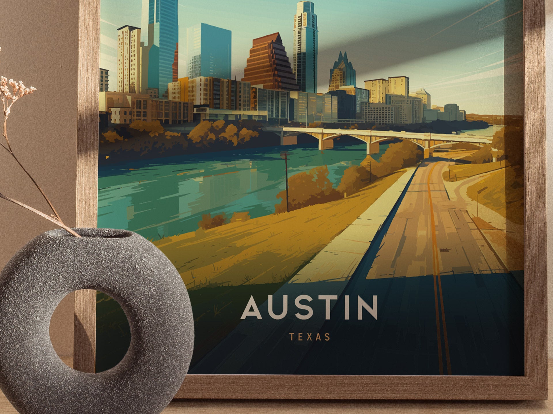 A vibrant illustration of Austins skyline with modern buildings, a bridge over a river, and a road in the foreground. A textured round vase sits beside the framed print.