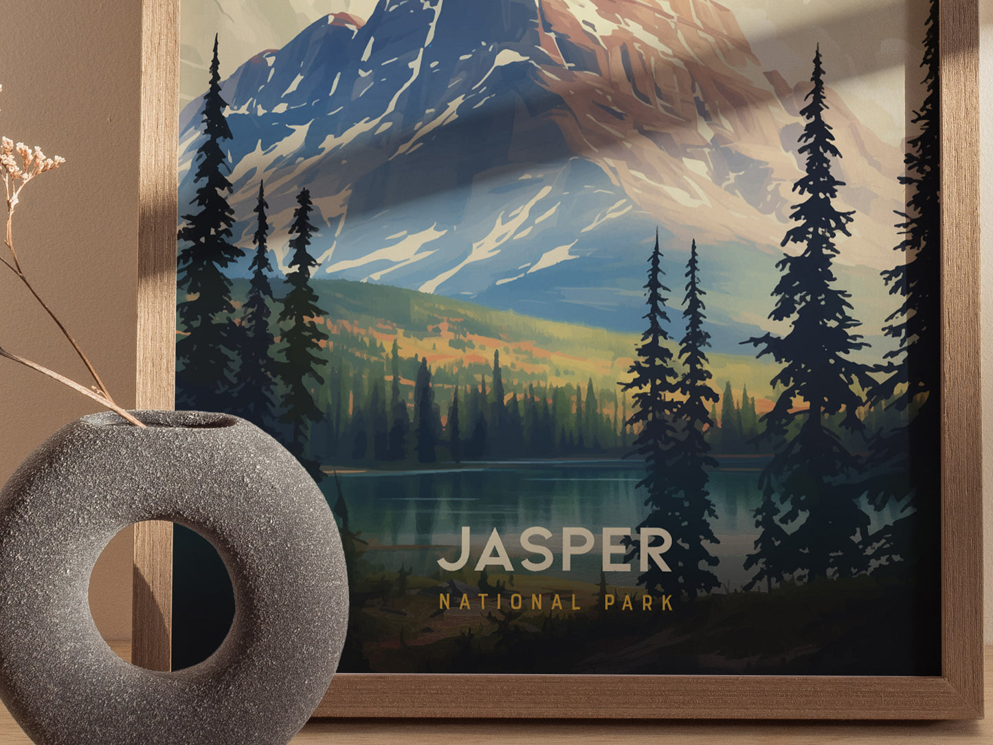 A framed poster of Jasper National Park features a scenic landscape with towering mountains, evergreen trees, and a tranquil lake. A textured gray vase with dried flowers sits nearby.