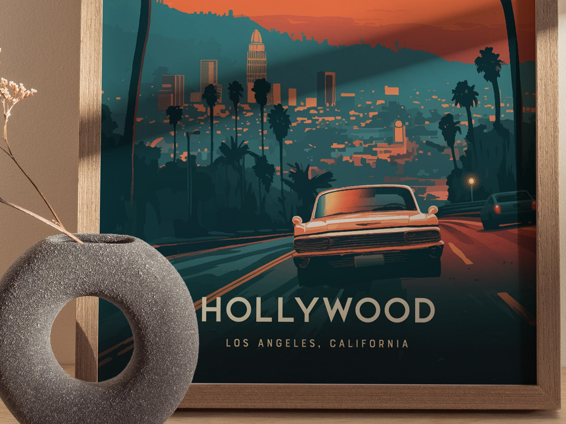 A framed poster depicts a vintage car driving towards a stylized Los Angeles skyline with palm trees and city lights. A textured circular vase sits beside the artwork.