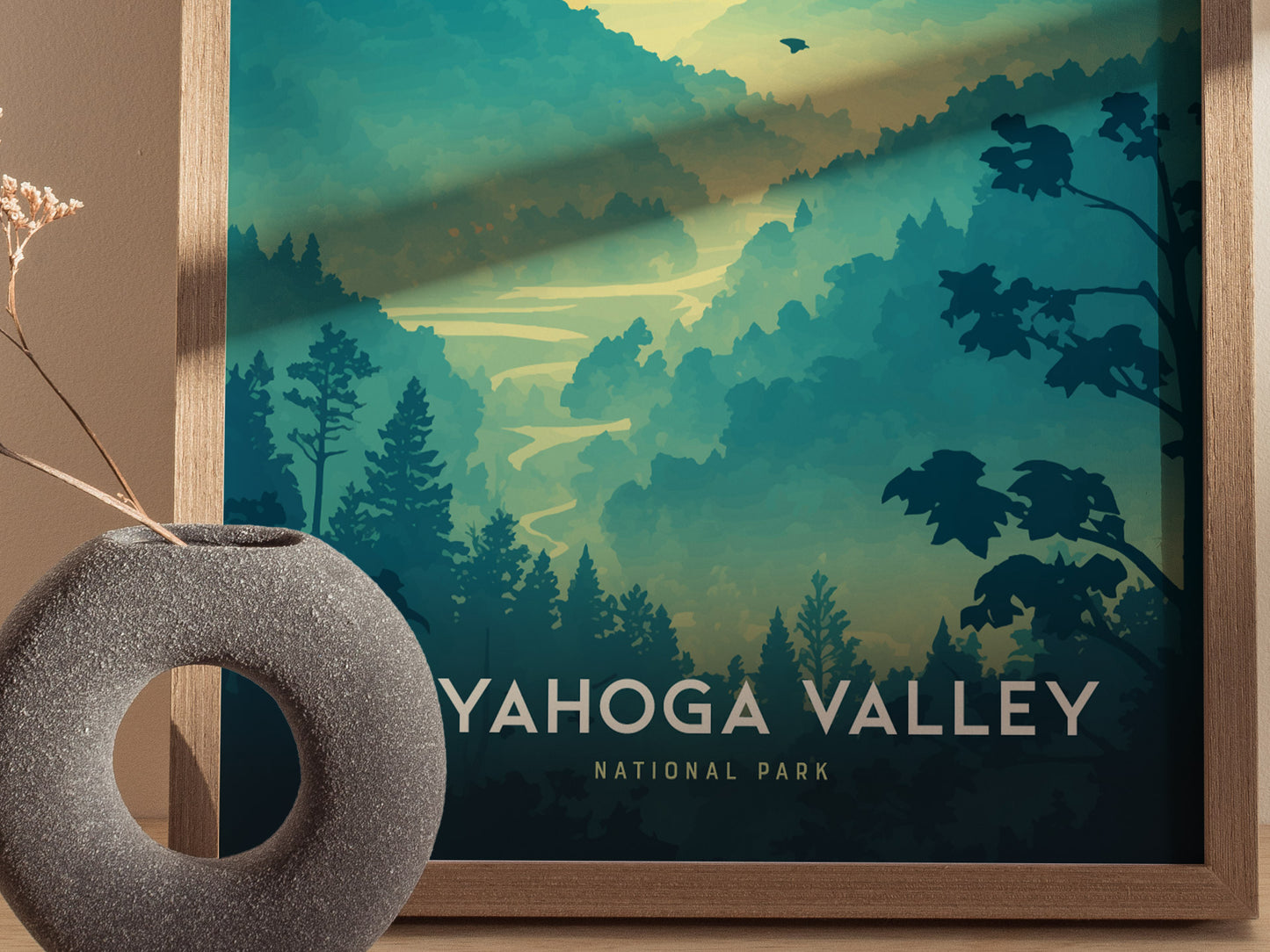 A framed poster of Cuyahoga Valley National Park features a stylized landscape with layered green hills and trees. A textured gray vase with dried flowers is placed in front.