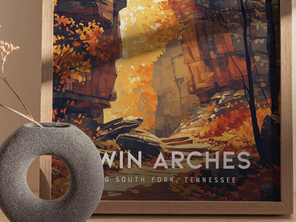 A framed poster of Twin Arches in Big South Fork, Tennessee, displays vibrant autumn foliage and sandstone formations. A textured, circular vase with dried plants is in the foreground.