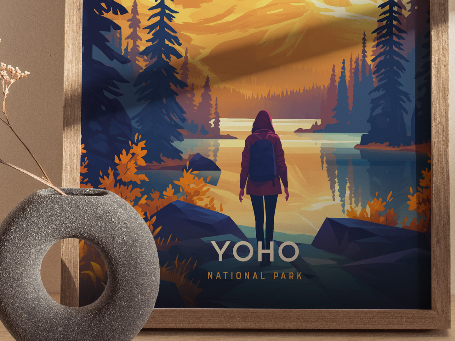 A person in a red jacket stands by a tranquil lake surrounded by pine trees and mountains at sunset. The text Yoho National Park is visible on the poster.