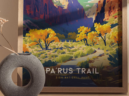 A framed poster depicts a vibrant illustration of Zion National Parks Parus Trail, featuring colorful autumn trees and majestic canyon walls. A textured stone vase is in the foreground.