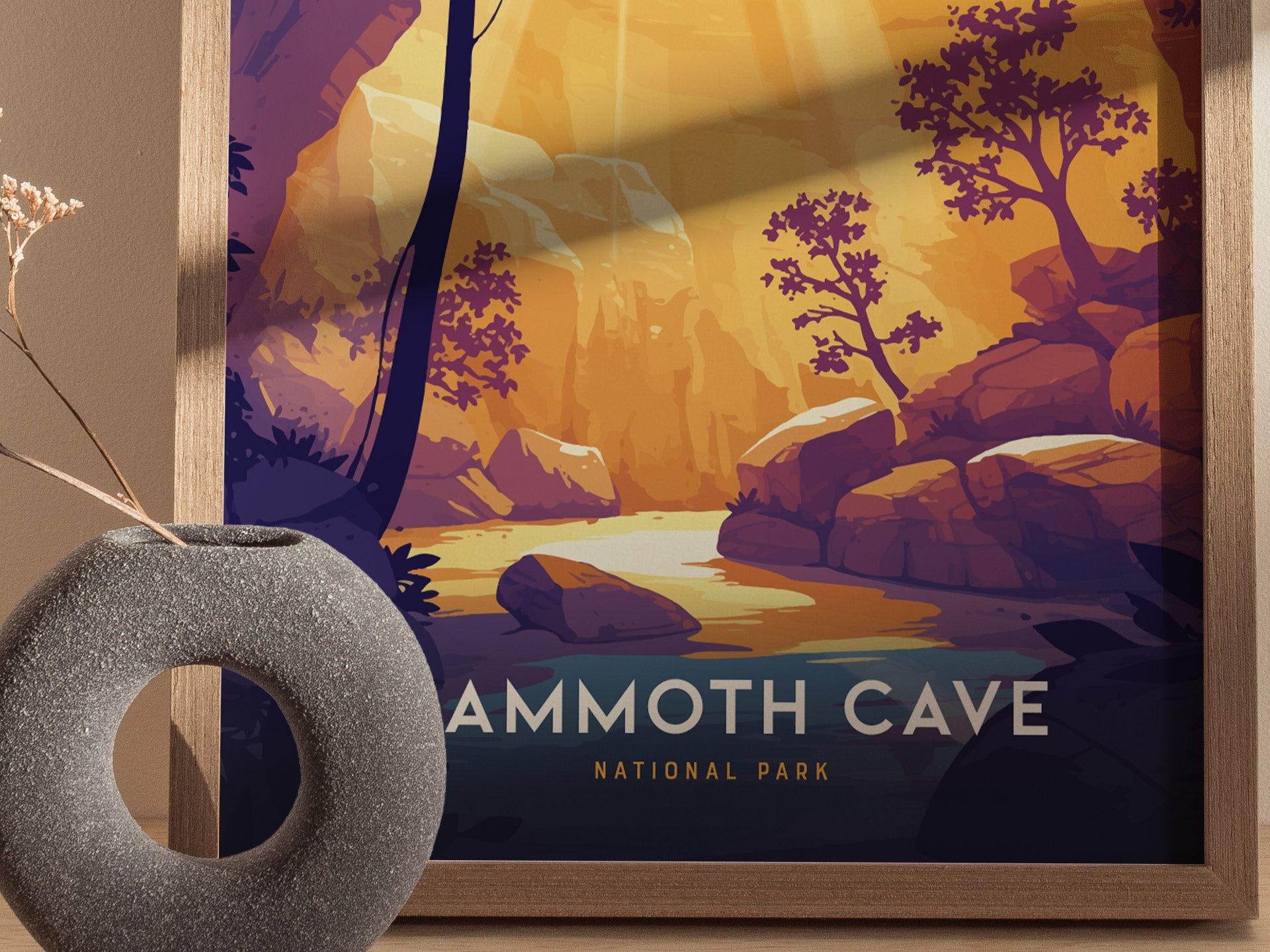 A framed Mammoth Cave National Park poster features an illustrated landscape with rocky formations and trees under warm lighting. A round gray vase with dried stems sits nearby.