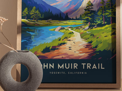 A colorful John Muir Trail poster depicts a scenic path with lush greenery, a tranquil blue lake, and distant mountains. A textured round vase with dried flowers accents the composition.