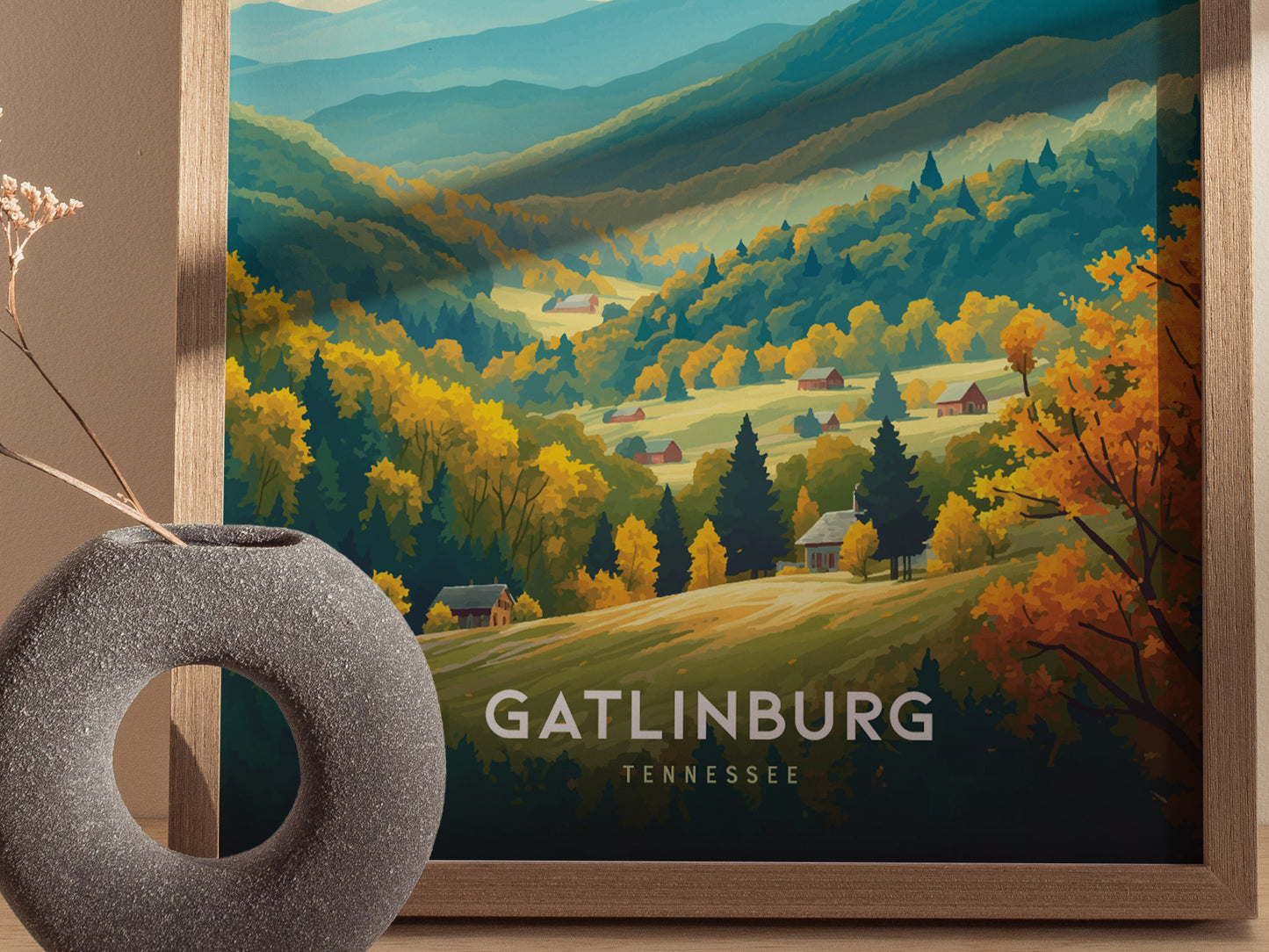 A vibrant poster of Gatlinburg, Tennessee, features lush, colorful mountains and valleys with scattered houses, framed in wood. A round, textured vase sits in the foreground.