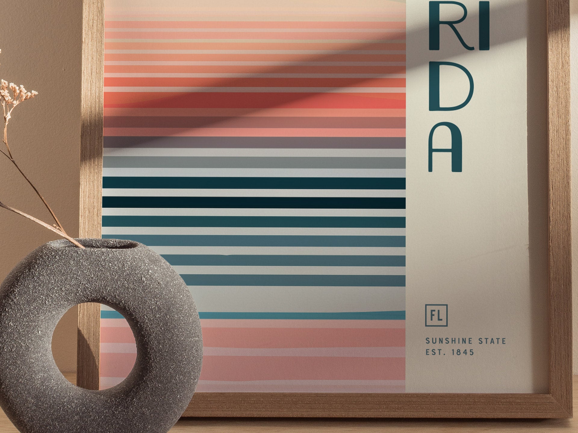 A framed poster with horizontal pastel stripes in shades of pink and blue, featuring the word FLORIDA and a modern vase in the foreground.