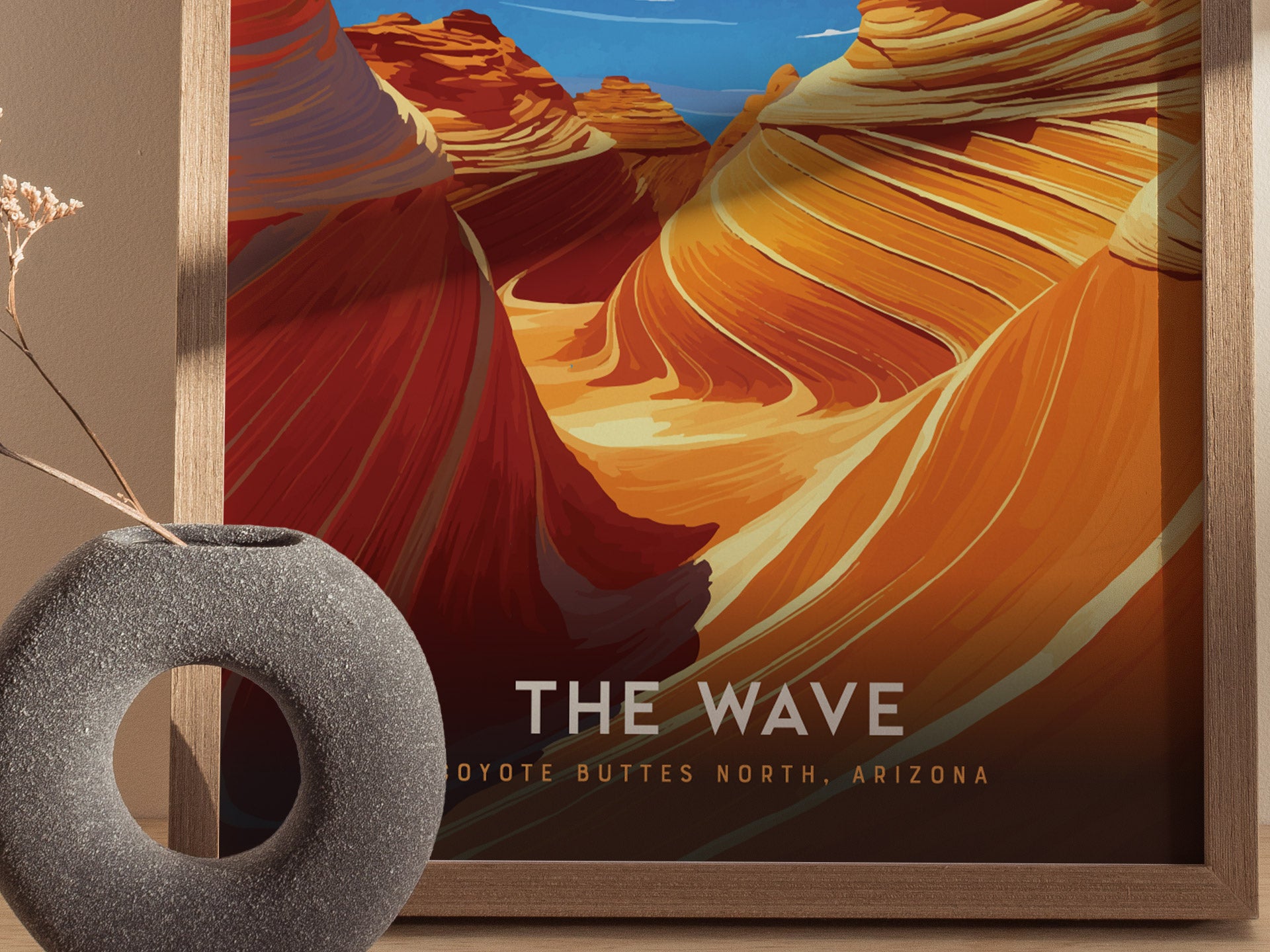 A framed poster of The Wave in Coyote Buttes, Arizona, showcasing vibrant swirling sandstone formations. A textured round vase with dried flowers is in the foreground.