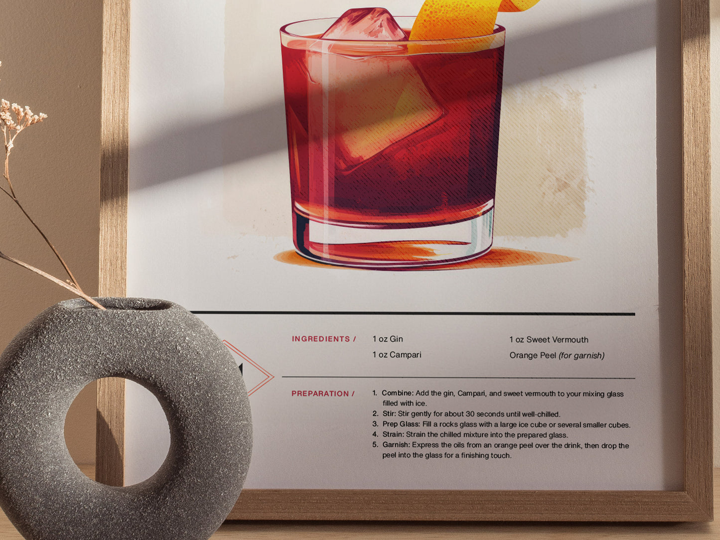 A framed poster features a stylized illustration of a Negroni cocktail with an orange peel garnish. A round, textured stone vase with dried flowers is placed nearby.