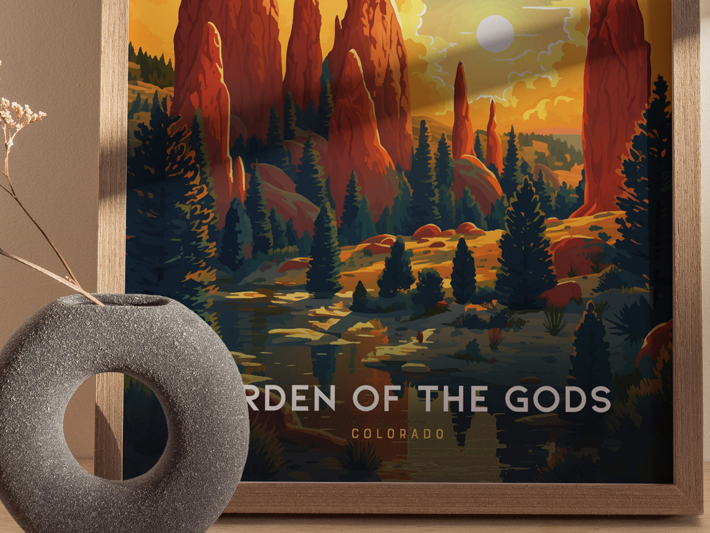 Framed artwork depicting the Garden of the Gods with vibrant red rock formations and silhouetted trees under a dramatic sky. A decorative round vase sits in the foreground.