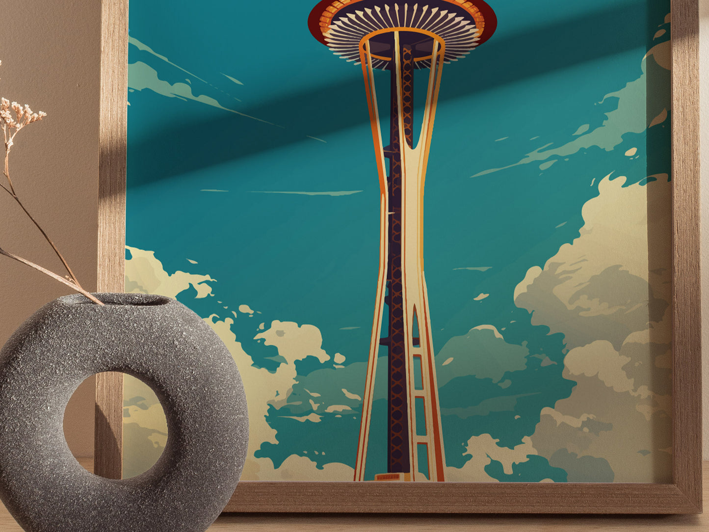 A framed poster of the Space Needle against a blue sky with clouds, alongside a textured stone vase with dried flowers.