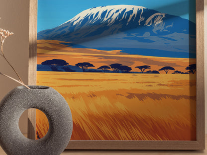 A framed poster of Mount Kilimanjaro with a snow-capped peak and savanna landscape. A grey, circular vase with dried flowers is placed in the foreground.