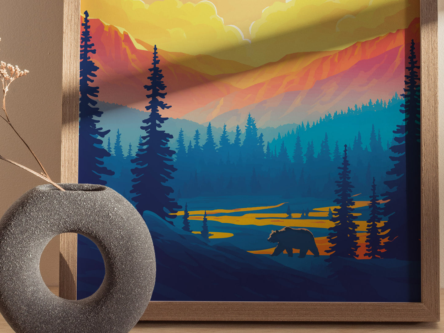A framed poster depicting a colorful landscape of Yellowstone National Park with a bear silhouette and vibrant sunset hues. A textured round vase with dried flowers is in the foreground.